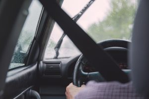 Interior view of a car during rainy weather, emphasizing safety with visible seat belt and driver focused on road. Vue intérieure d'une voiture par temps pluvieux, mettant l'accent sur la sécurité avec une ceinture de sécurité visible et le conducteur concentré sur la route.