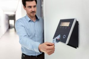 Professional man using access card on wall reader in office setting. Un homme professionnel utilisant une carte d'accès sur un lecteur mural en milieu de bureau.