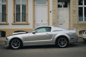 A sleek silver Mustang parked in front of classic urban architecture. Une élégante Mustang argentée garée devant une architecture urbaine classique.