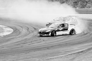 High-speed car drifting action on a racetrack in monochrome for dynamic motorsport thrills. Action de dérive haute vitesse d'une voiture sur un circuit de course en monochrome pour des sensations fortes de sport automobile dynamique.