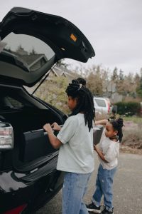 Two young siblings help each other load luggage into a car trunk for a family trip. Deux jeunes frères et sœurs s'aident mutuellement à charger les bagages dans le coffre d'une voiture pour un voyage en famille.